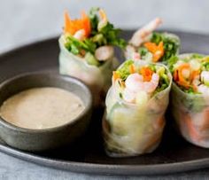 several rolls with shrimp and carrots on a black plate next to a dipping sauce