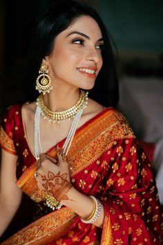 a woman in a red and gold sari with pearls on her neck, smiling at the camera