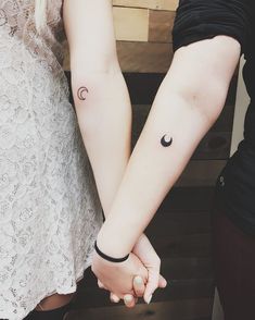 two people holding hands with tattoos on their arms and one has a crescent moon tattoo