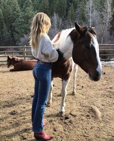 a woman standing next to a brown and white horse on top of a dirt field