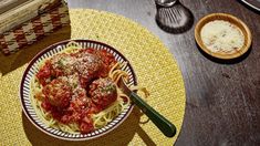 a bowl of spaghetti with meatballs and sauce on the table next to a book