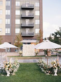 an outdoor wedding setup with umbrellas and flowers on the grass in front of a building