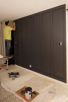 a man standing on top of a wooden floor next to a black cabinet in the middle of a room