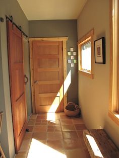 the sun shines through the window onto a hallway with two wooden doors and a bench