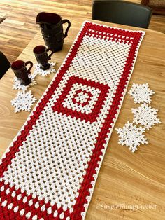 a crocheted table runner with coffee mugs on it and snowflakes