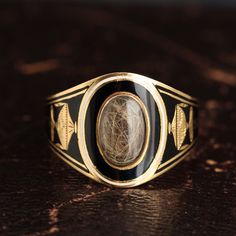 This 18k gold and enamel Georgian mourning ring is modeled in a cigar band shape with a hair locket at the face. The enameling technique used to make a ring like this is called champlevé. This method required the jeweler to cut away the gold of the band to form shapes, letters or numbers, fill the recessed space with powdered enamel, fire the ring at a high enough temperature to liquefy the enamel, and then let it cool to the glassy hardened state you see here. This ring is decorated with exquis 1800s Jewelry, Hair Locket, Victorian Hair, Georgian Ring, Georgian Jewelry, Dope Jewelry, Colored Gems, Memento Mori, Enamel Jewelry