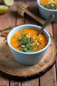 two bowls of carrot soup on a wooden board with spoons and lemon wedges