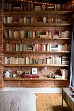 a bookshelf filled with lots of books next to a brick wall and wooden floor