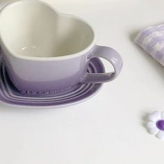 a white and purple heart shaped dish set on a table next to a napkin with flowers