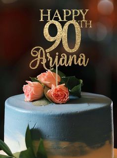 a blue cake with gold lettering and two pink roses on top is sitting on a table