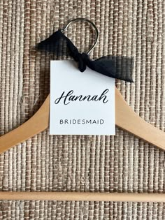 a wooden hanger with a name tag on it and a black ribbon attached to the hanger