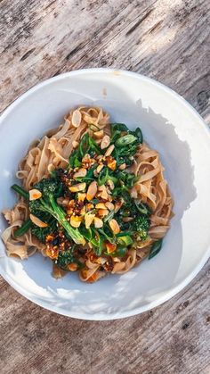 a white bowl filled with noodles and vegetables on top of a wooden table next to a fork