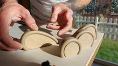 a man is making wooden toys on a table in front of a fenced yard