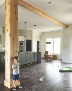 a young boy standing in the middle of an empty living room with wood beams on the ceiling