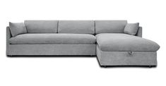 a gray sectional couch sitting on top of a white floor next to a footstool