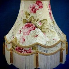 a lamp shade with pink flowers and fringes on the bottom, against a blue background