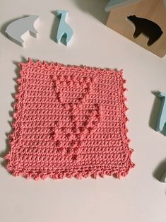 a pink crocheted square sitting on top of a table next to cut up letters