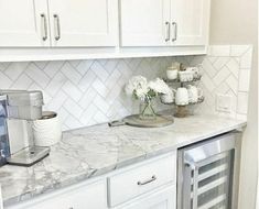 a white kitchen with marble counter tops and stainless steel appliance on the side