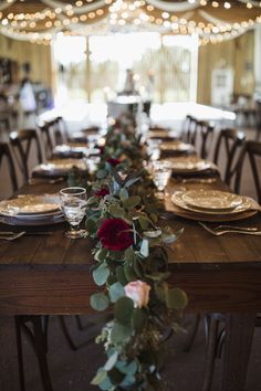 a long table with plates and flowers on it in a room filled with tables set for dinner