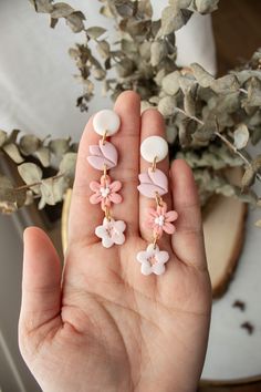 a person is holding their hand up to some flowers on the earrings that are hanging from them