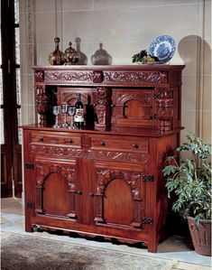 a wooden cabinet with carvings on the front and sides, sitting next to a potted plant