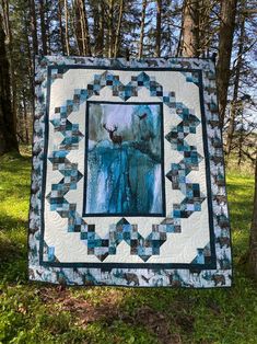 a blue and white quilt hanging on a tree in the woods with trees behind it