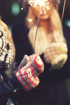 two women holding sparklers in their hands while wearing mittens and gloves with them