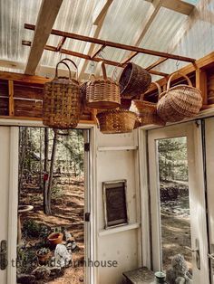 several baskets hanging from the ceiling in a room with glass walls and doors leading to a wooded area