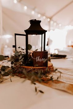 a lantern on top of a table with greenery around it and a sign that says three