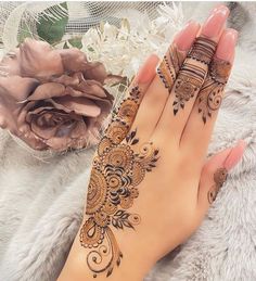 a woman's hand with henna tattoos on it and flowers in the background