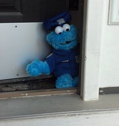 a blue stuffed animal wearing a hat and uniform sitting on the front step of a house