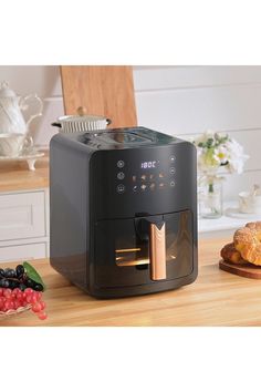 a black coffee maker sitting on top of a wooden table next to fruit and bread