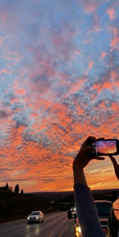 a person taking a photo with their cell phone on the side of the road at sunset