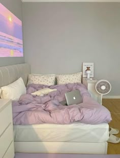 a bed with a laptop on top of it in a bedroom next to a fan