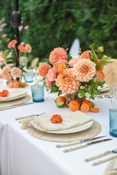 the table is set with plates, napkins and vases filled with orange flowers