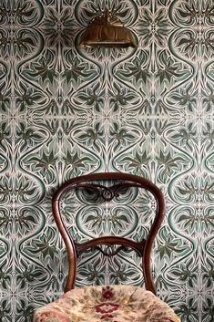 a chair and lamp in front of a wall with an ornate pattern on the back