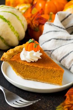 a slice of pumpkin pie on a white plate with whipped cream and orange pumpkins in the background