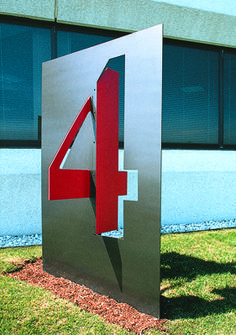 a metal sign with the number four on it in front of a building and grass