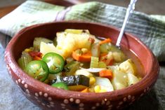 a red bowl filled with vegetables on top of a table next to a green towel