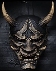 a mask with horns on it is shown in black and gold colors, against a dark background