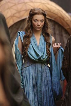 a woman with long hair standing in front of other people wearing medieval clothing and holding an umbrella