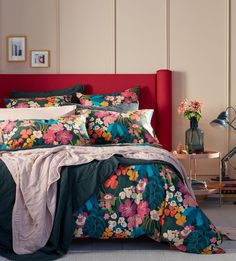 a bed with colorful flowers on it in a room next to a red headboard