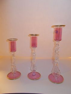 three pink candlesticks sitting on top of a white table next to each other