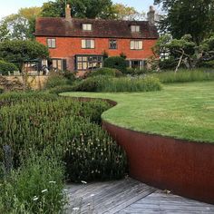 a large red brick house sitting on top of a lush green field next to a wooden deck