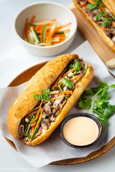 two sub sandwiches sitting on top of a wooden tray next to bowls of vegetables and dipping sauce