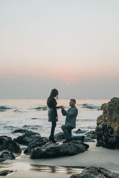 a man kneeling down next to a woman on top of a rock near the ocean