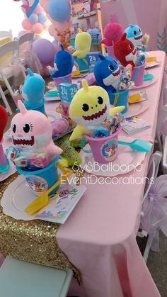 a pink table topped with lots of toys and balloons in the shape of shark's teeth