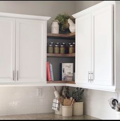 a kitchen with white cupboards and shelves filled with spices, utensils and books