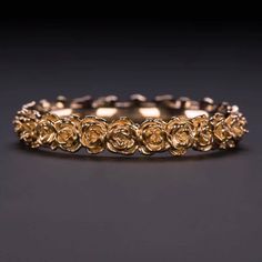 a yellow gold ring with flowers on it, sitting on a black surface in front of a dark background