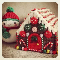 a crocheted gingerbread house next to a knitted snowman with a red hat